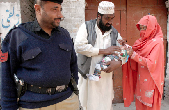 Image of oral vaccine being administered to an infant while a police officer looks on.