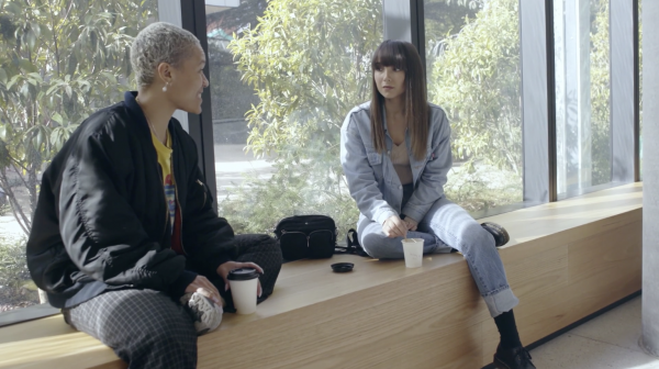 Two students sit beside a window chatting and drinking coffee.