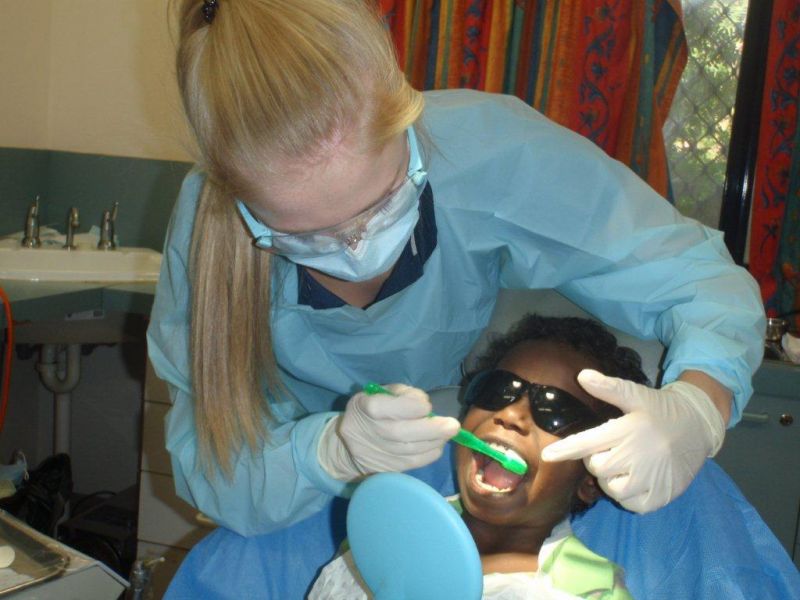 Oral health student looking in the mouth of an Aboriginal child sitting in a dental chair