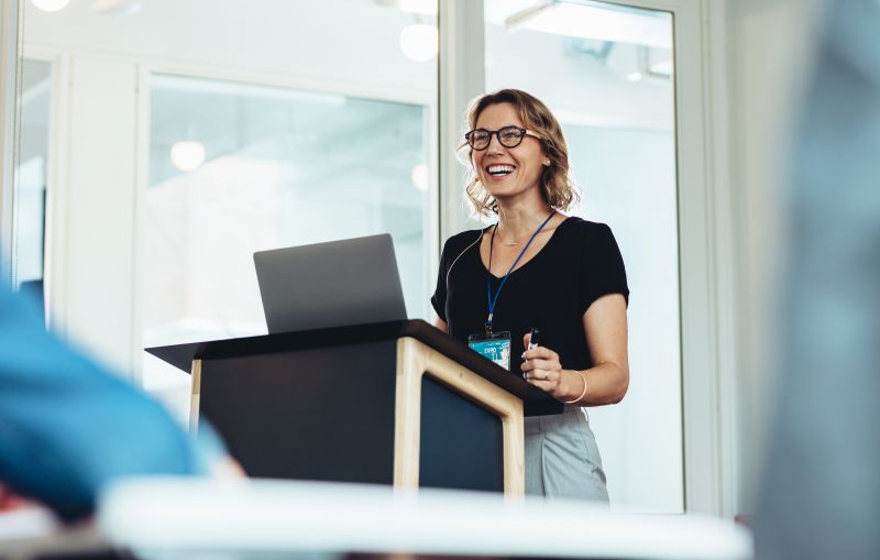 A woman standing at a lectern presenting to the room