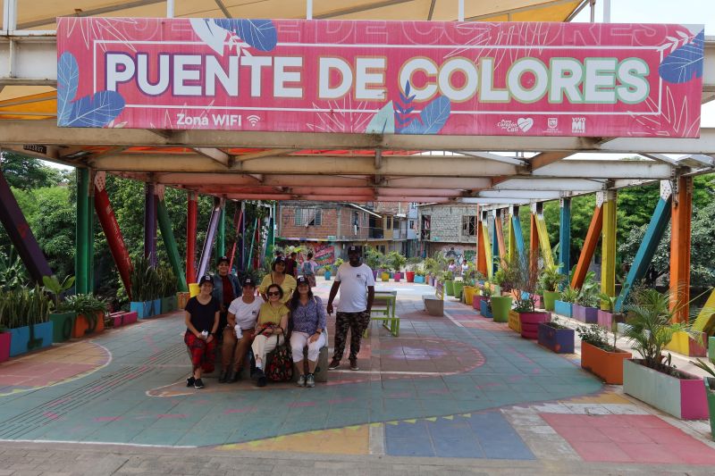 A group of people sitting on a bench upon a colourful bridge