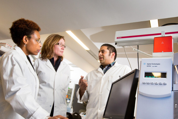 Three people standing in a lab in conversation.