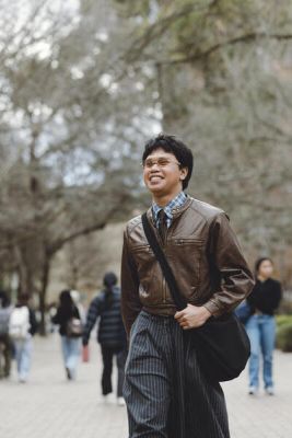A student walks along a busy walkway with a smile on his face.