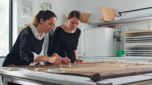 Two women painting on fabric.