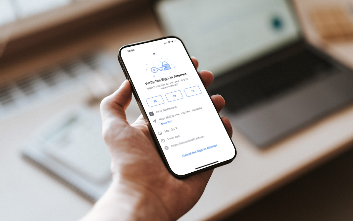 A photo of someone holding a phone with the Okta MFA push notification on screen