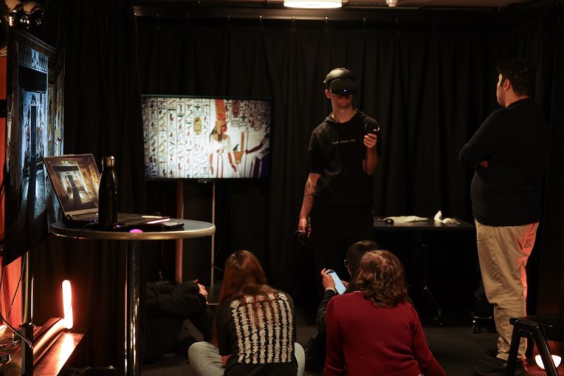 A group of students wearing virtual reality goggles explore ancient Egyptian history in a lab, with screens reflecting what they see through the goggles. 