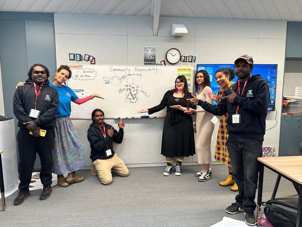 A diverse group of people smiling and posing in front of a whiteboard filled with notes and diagrams.