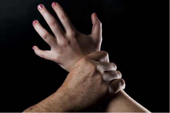 Image of a male hand gripping a female hand agressively.
