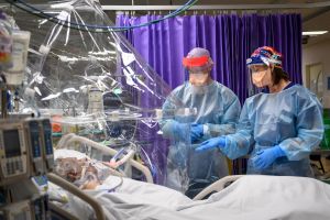 Patient in medihood to protect hospital staff from covid. Healthcare workers by hospital bedside