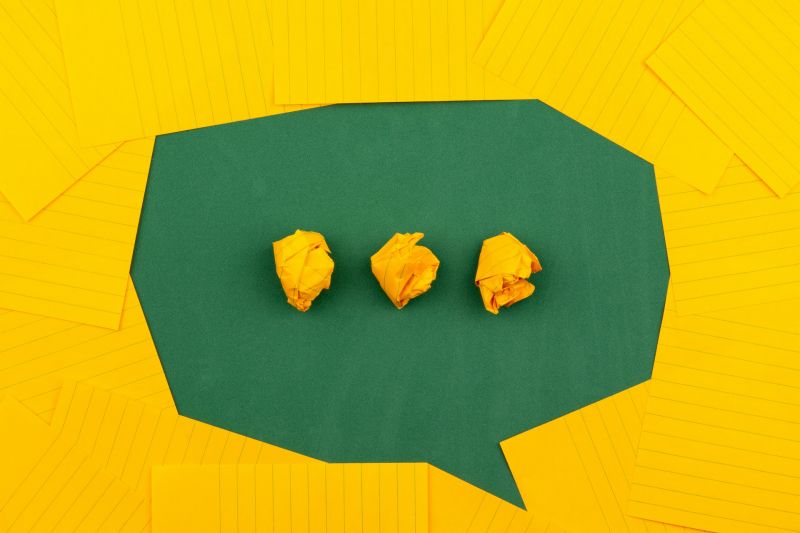 A green speech bubble made of paper on a yellow background