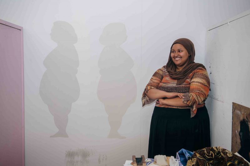Student artist Naimo Omar stands in front of artwork