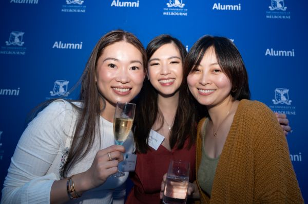 Three friends taking a photo in front of a University of Melbourne photo wall at the reunion event.