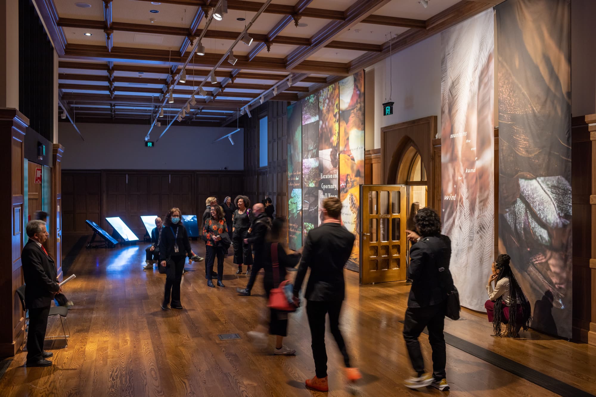 People walk through Old Quad gallery with screens on floor in background