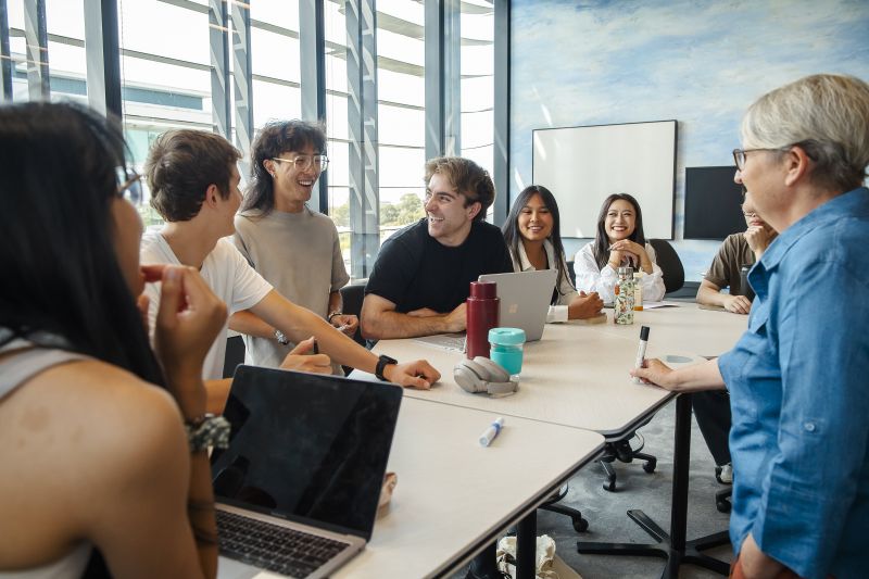 Students sitting at a desk, talking and discussing with their lecturer.