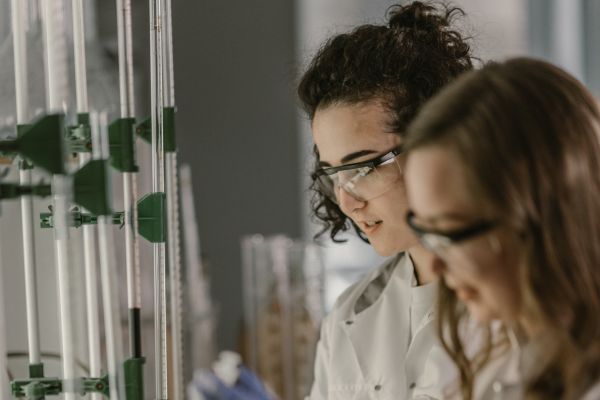 People in lab coats and safety glasses looking at scientific equipment.