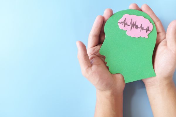 person holding green and pink paper cut out shape of a human head and brain, over a sky blue background.