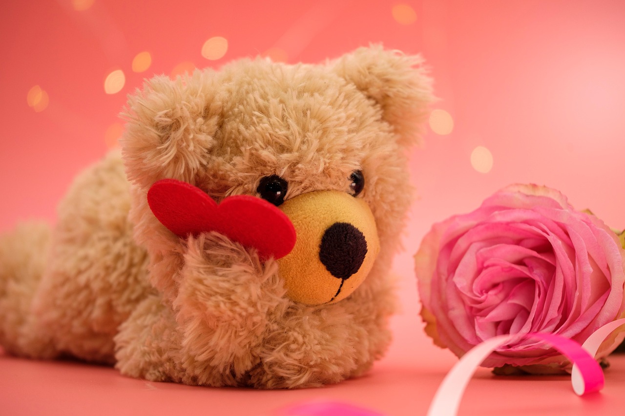 Teddy bear holding a love heart next to a pink rose