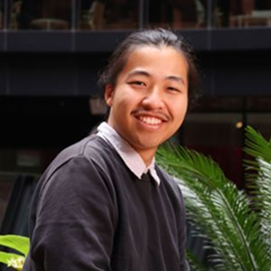 A young student wearing a shirt under a jumper smiling to camera.
                                class=