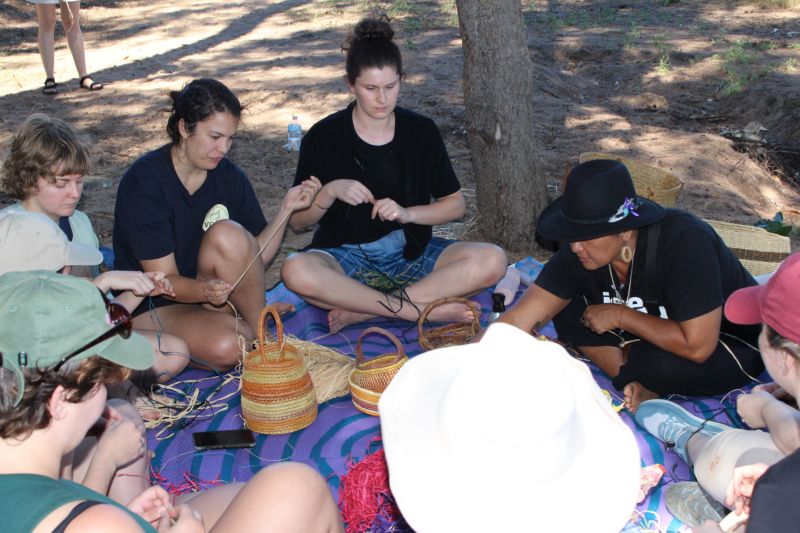 Participants of the On Country subject sitting on the sand weaving traditional baskets