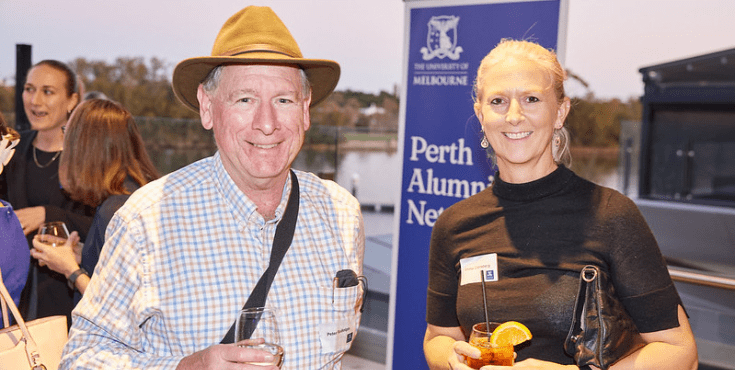 A man and woman holding drinks on a rooftop. The banner behind them reads 'Perth alumni network'.