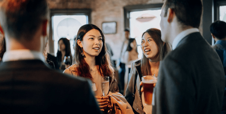 Two Korean alumni laughing and chatting with drinks in hand.