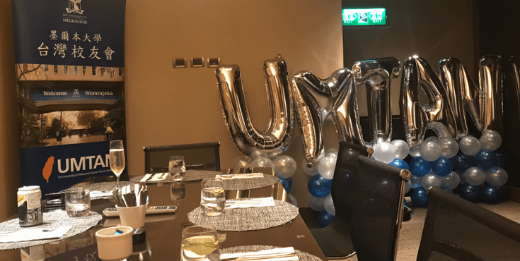 A table set with placemats and drinks, with balloons and decorations in the background.