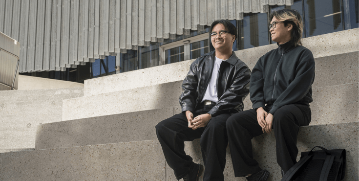 Two students wearing black smiling and seated on steps.