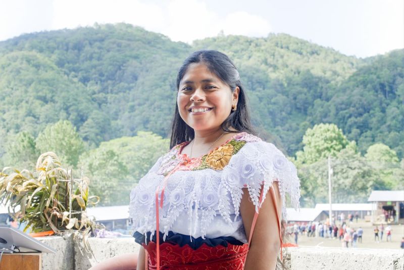 A woman smiles while standing in front of a small hill.