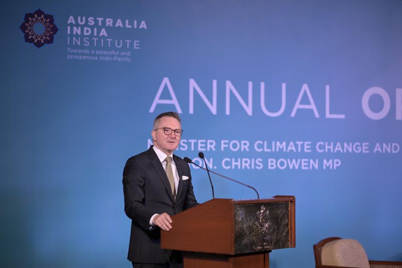 Person speaking at a lectern during a formal event, with event branding displayed behind