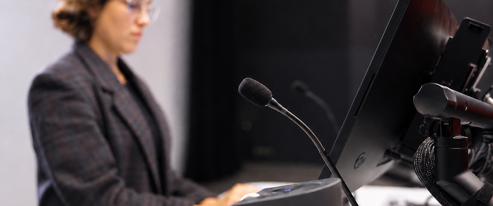 Lecturer presenting from a classroom lectern equipped with a microphone, display and AV technology. The image highlights presentation equipment commonly used in teaching spaces.