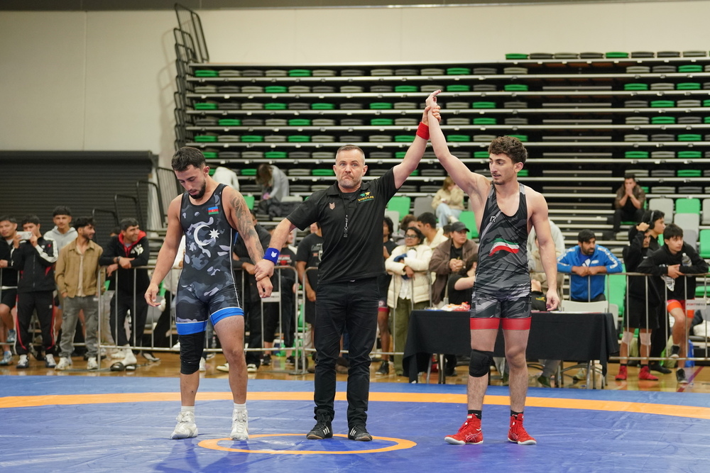 Two wrestlers celebrate victory by raising their hands in the air, showcasing their triumph in the match.