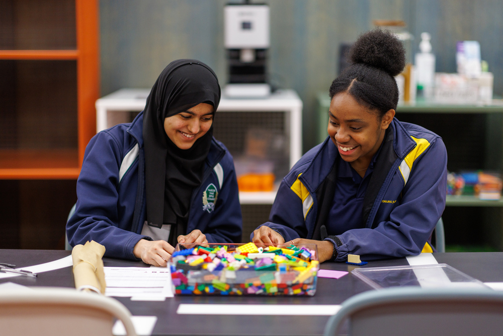 Two young women collaborate on a project at a classroom table.