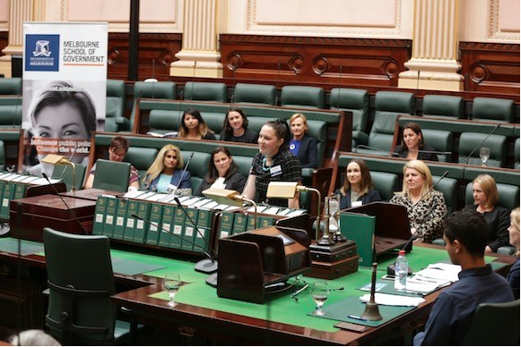 Image of Laura Chipp practicing a speech in the Victorian Parliament with other Pathways to Politics Fellows looking on.