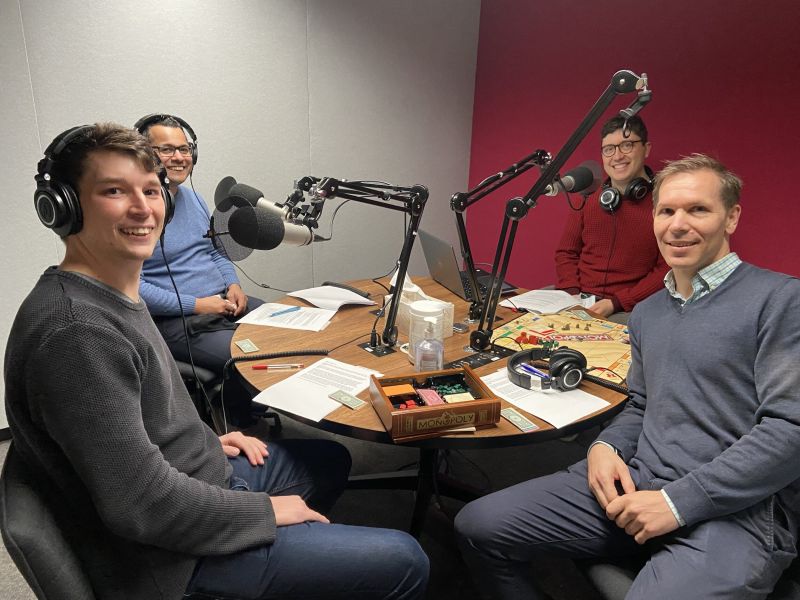 Four people sit in the podcast studio near microphones and are smiling at the camera.