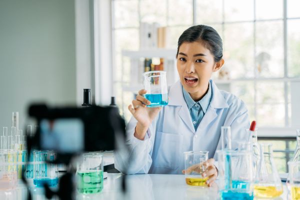 A lab with female scientist in white lab coat holds up blue liquid in a beaker.