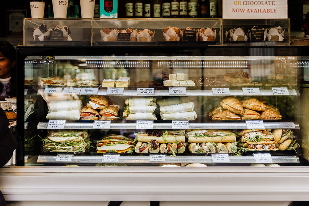 A glass cabinet displaying a variety of food options available including sandwiches and pastries