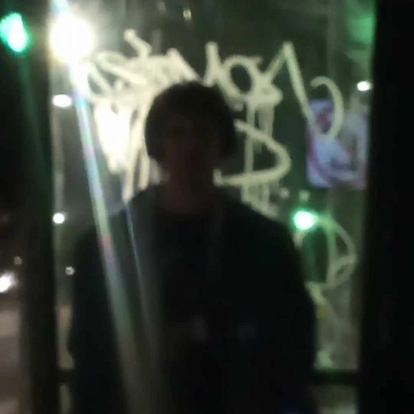 Quinn Franks is a silhouette against a glass with graffiti on it, and a light shining behind them.