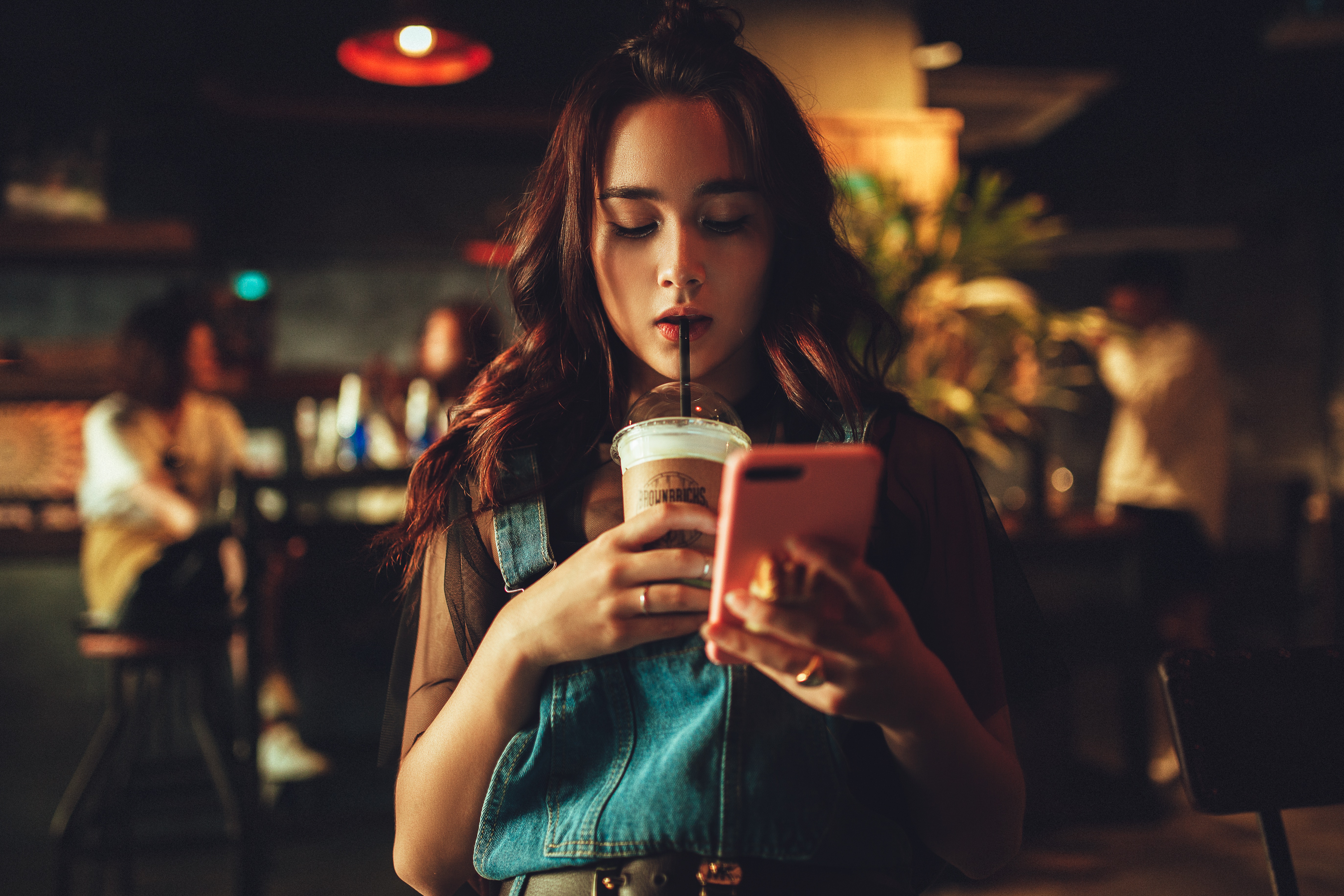 Woman looking at phone drinking a drink with a straw