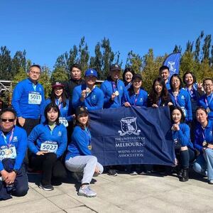 A group of Chinese alumni wearing matching blue jumpers posing together with a University of Melbourne flag.
                                class=