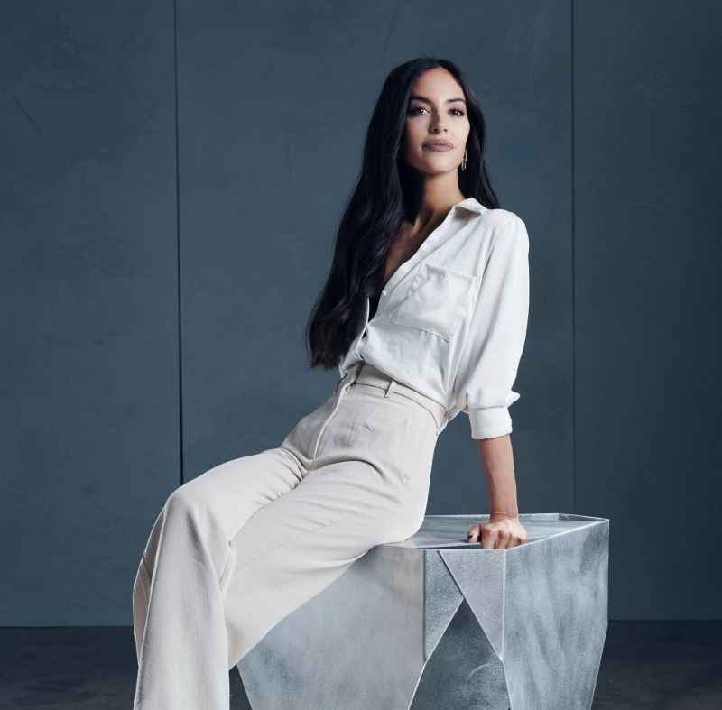 Dark haired woman wearing a white blouse and sitting on a plinth