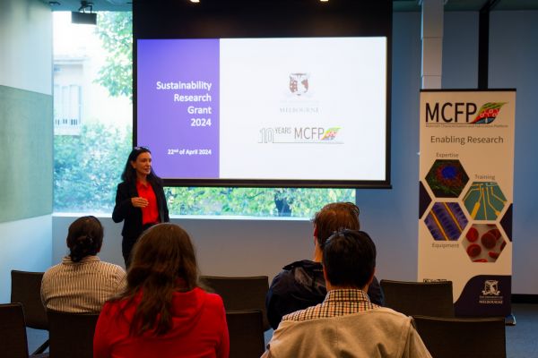 A dark haired woman presenting in front of a screen and audience of the MCFP Sustainability Grants event