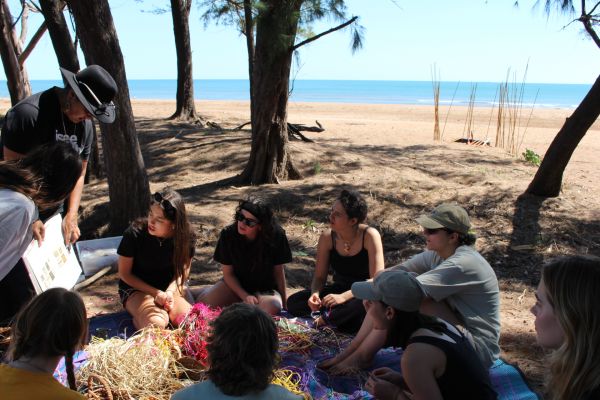 Participants of the Access to Justice On Country subject sit on a beach listening to their instructor