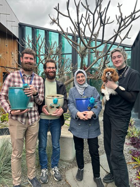 Four staff members holding pots and one holding a dog in a small courtyard with a tree behind them
