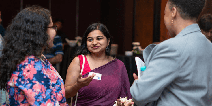 An Indian alum chatting with two other woman at an event.