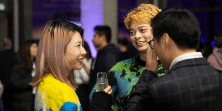 Three young alumni in colourful clothing chatting at an Arts-China Connect event. 