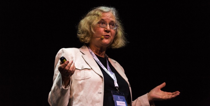 Elizabeth Blackburn speaking on stage with a presenter pointer in hand and a headset microphone.