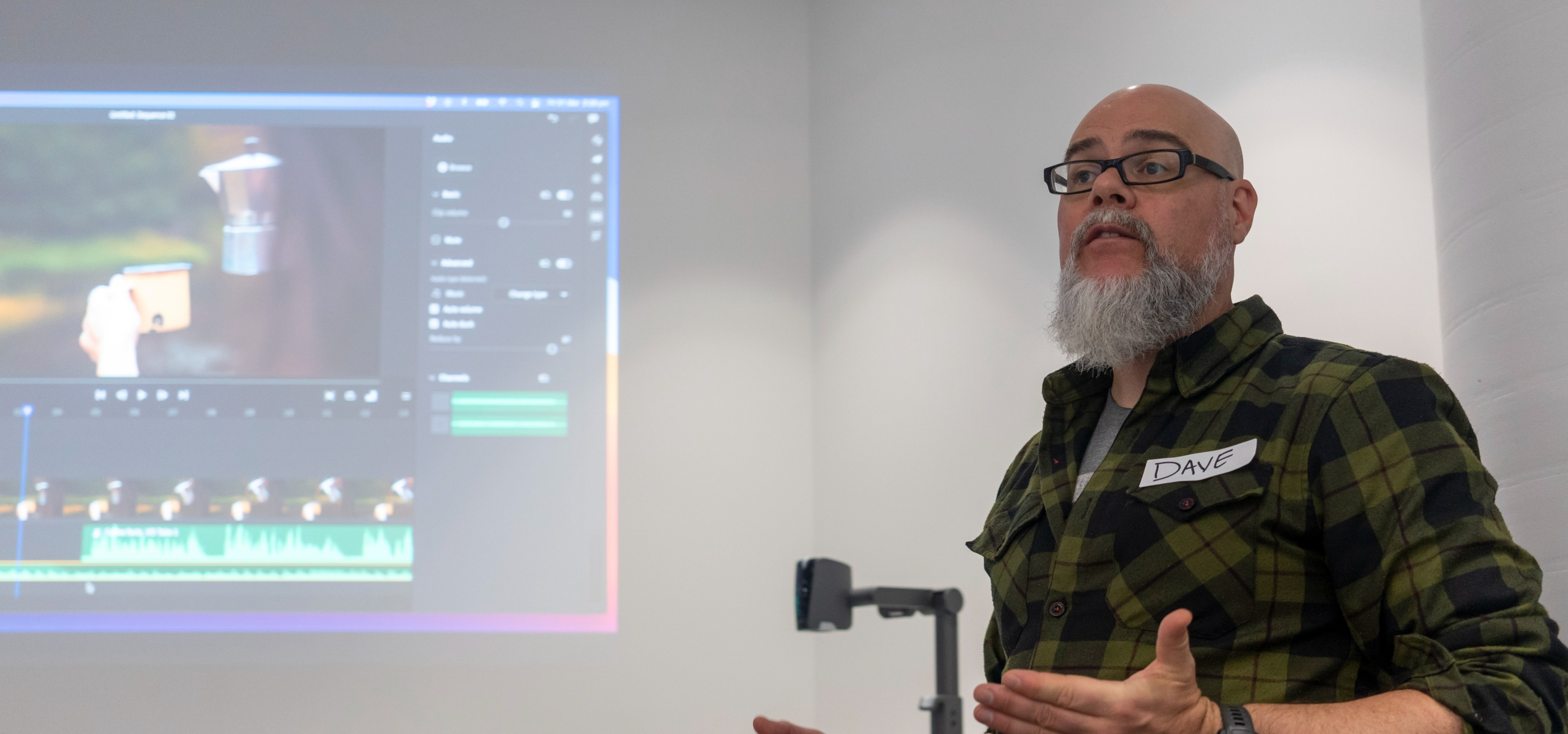 A man stands in a classroom in front of a slide in the midst speaking to his audience