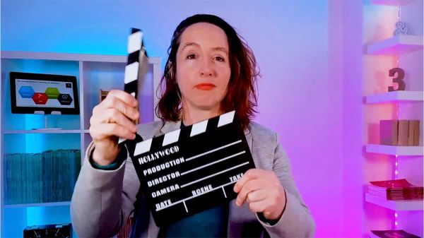 Woman in a studio lit with neon lights holding a clapper board.