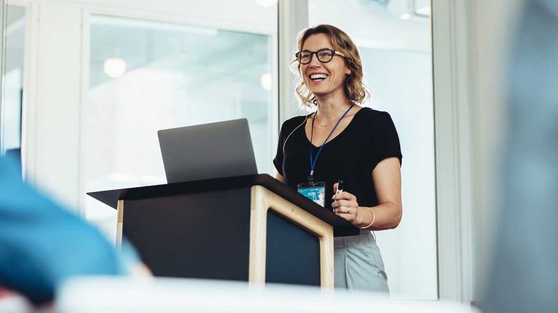 A female teacher lectures from a podium.