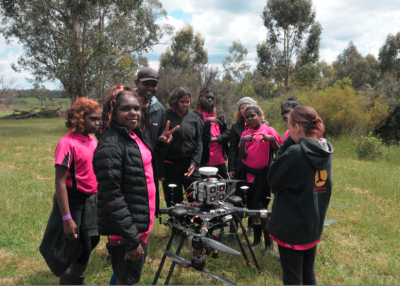 Image of Worawa students with an XM2 staff member pictured with a camera mounted on a drone.